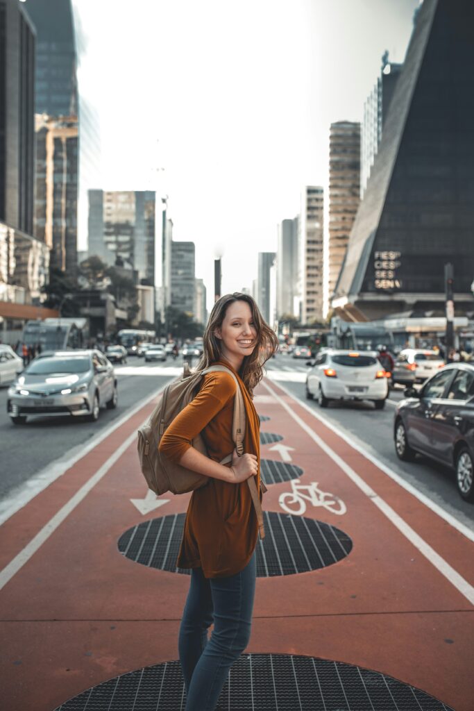 Una joven con una mochila sonríe mientras explora una nueva ciudad, con la emoción y la aventura de vivir en el extranjero.